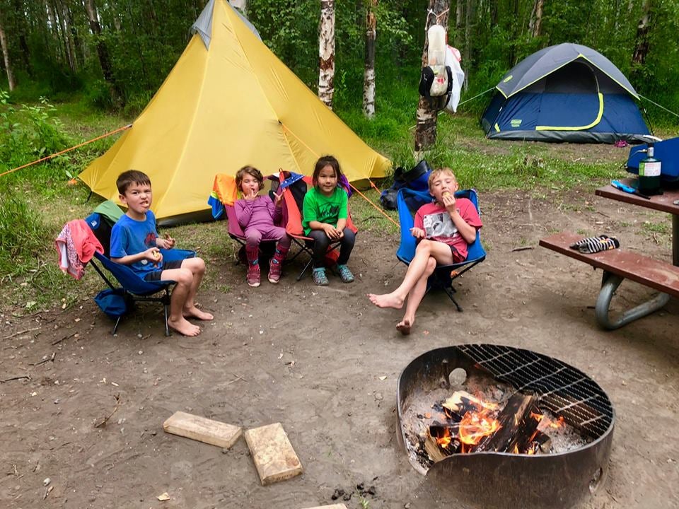kids gathered around a fire at a campsite in front of a tent