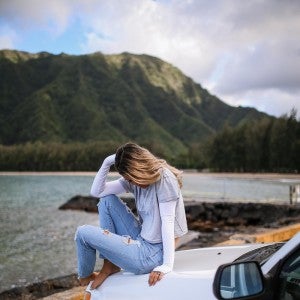 Women wearing eclipse glove sun protection sleeves while sitting on the hood of a car.