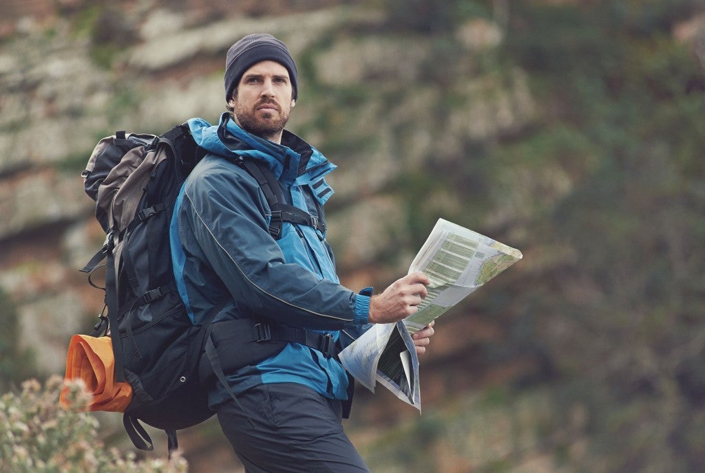 a man holding a paper map in the woods while hiking, looking confused