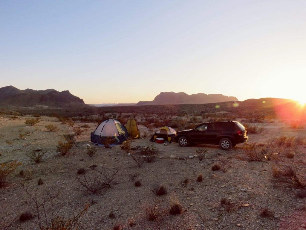 Tent pitched beside car in sandy desert.
