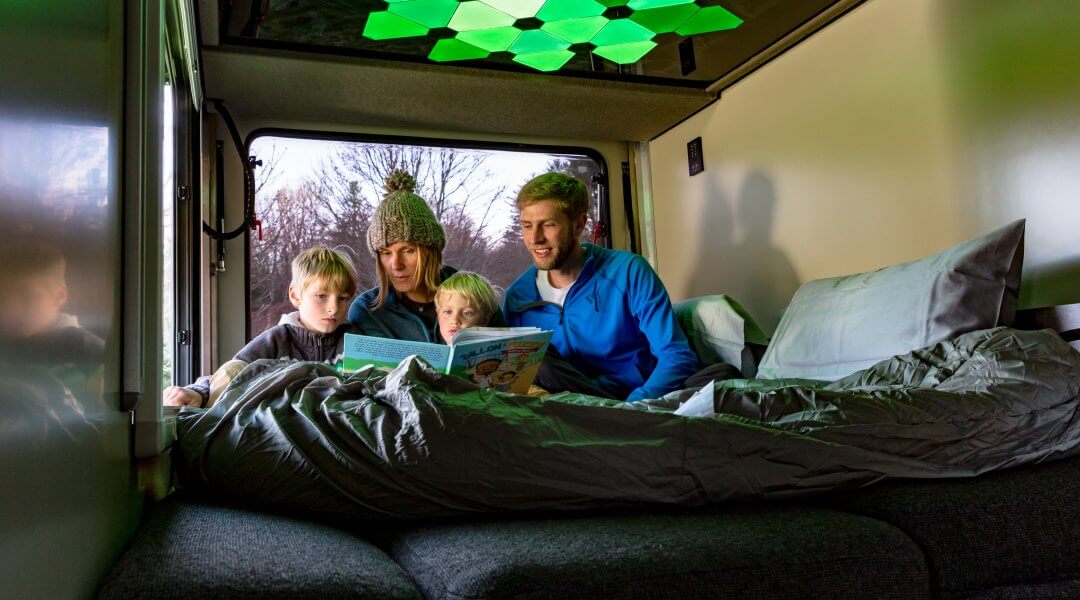 parents read a book to their two children beneath modern light panels in a camper