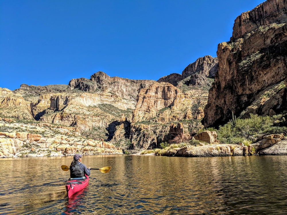 Woman in kayak paddling on lake with rocks in background.