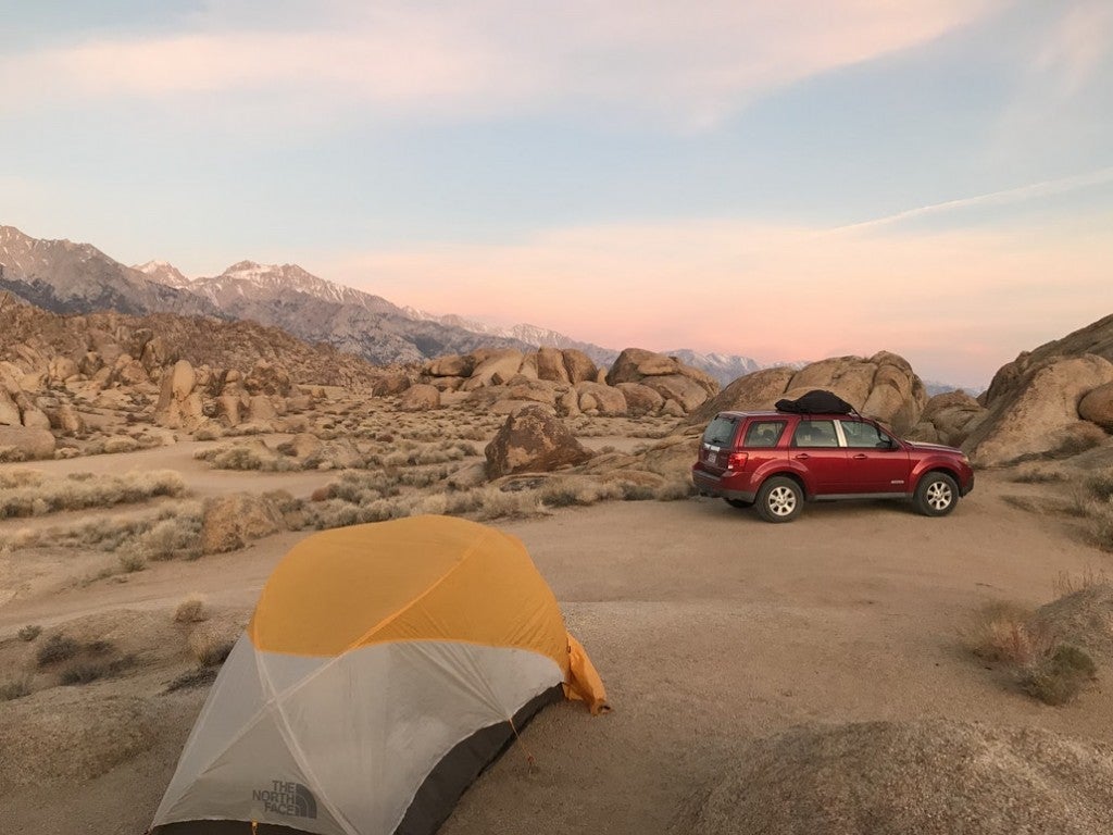 a red car and a tent set up between rocks in a desert in california