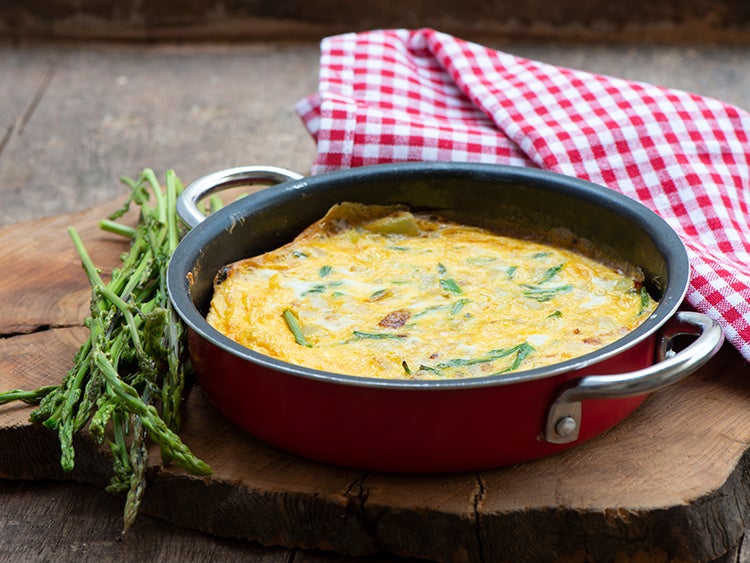 breakfast omelette in a skillet on wood plank surrounded by green sprigs and a gingham washcloth