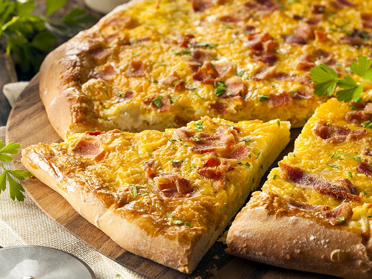 close up of a slice of breakfast pizza featuring eggs and bacon on crust