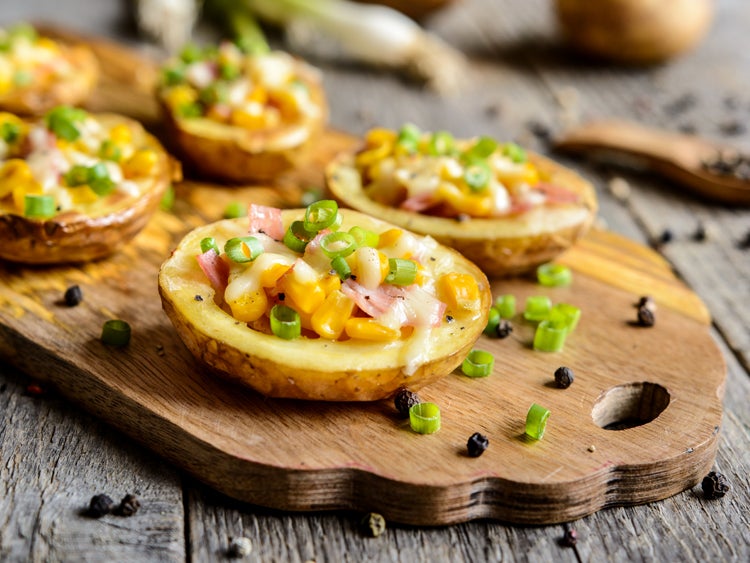 potato halves covered in breakfast ingredients like ham and scallions on a wooden serving tray