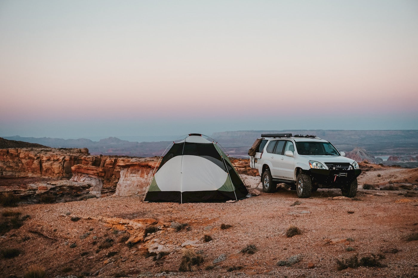 Tent pitched next to car parked in desert backcountry.