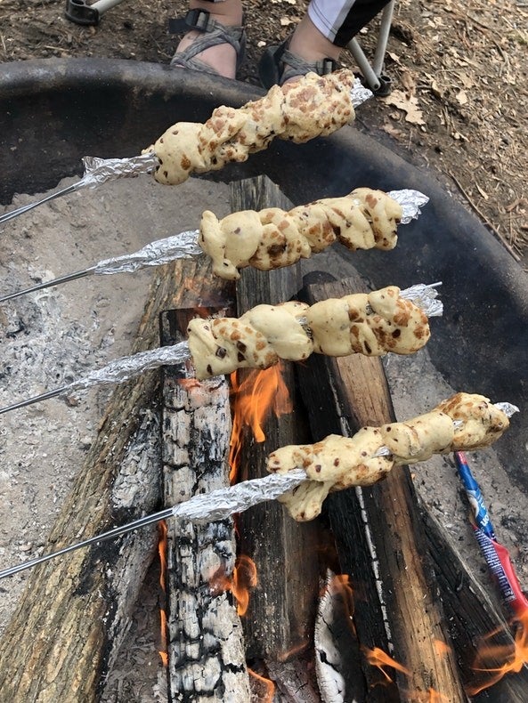 four skewers with dough over a campfire at daytime