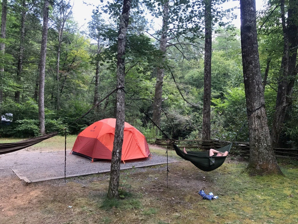 Guy reclining in hammock at a campsite.