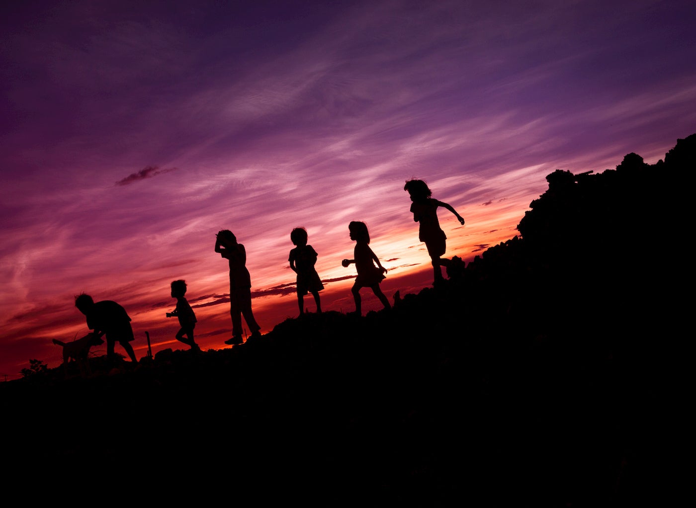 Silhouette of kids running downhill at sunset.