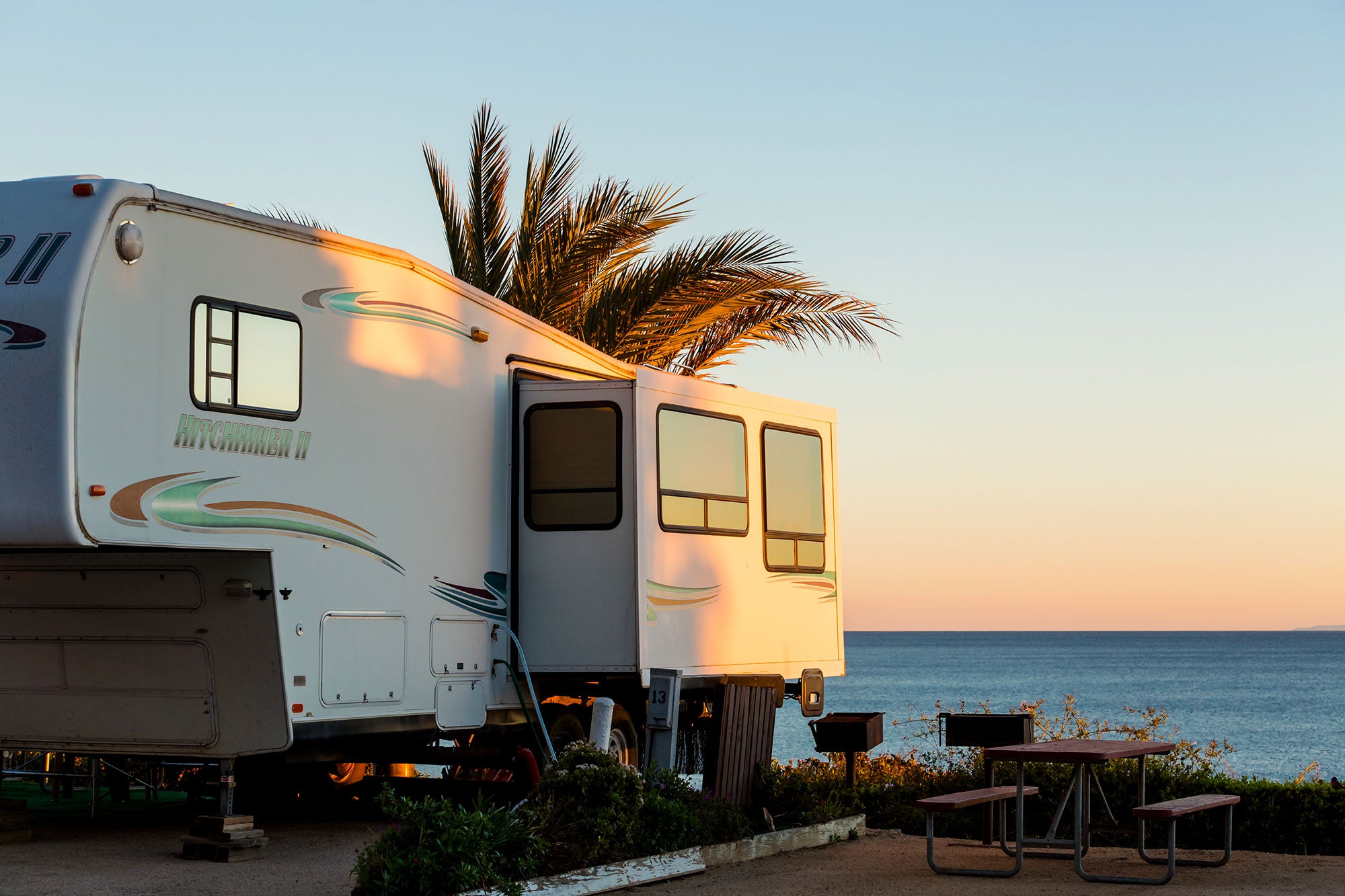 rv set up in beach campsite as the sun sets over the water