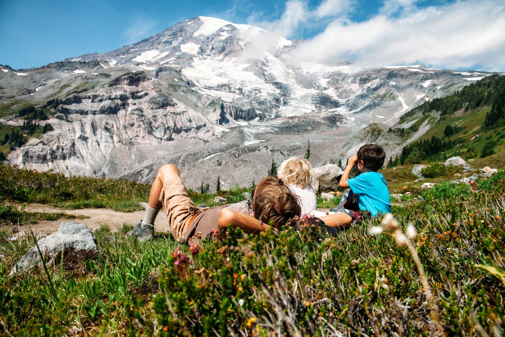 Father and kids laying in flowers with Mount Ranier in background 