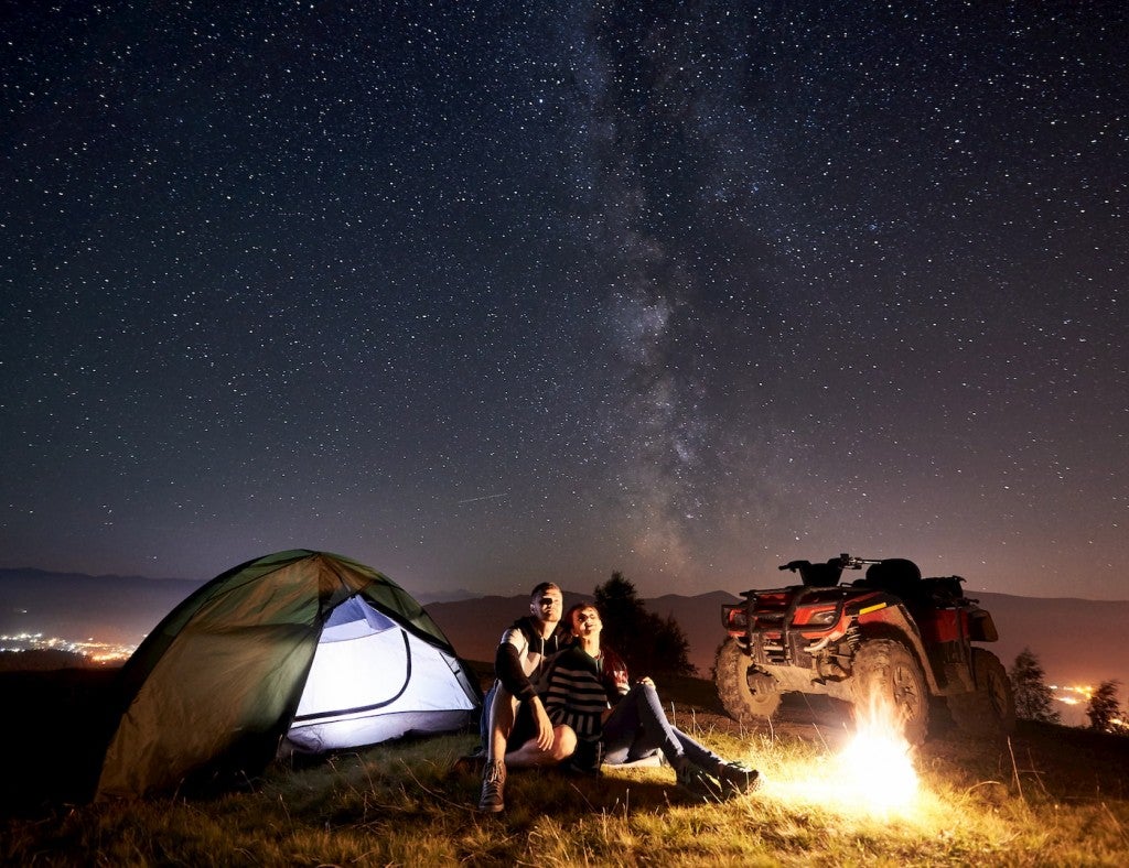 Couple hanging out by the fire beside a tent and 4x4.