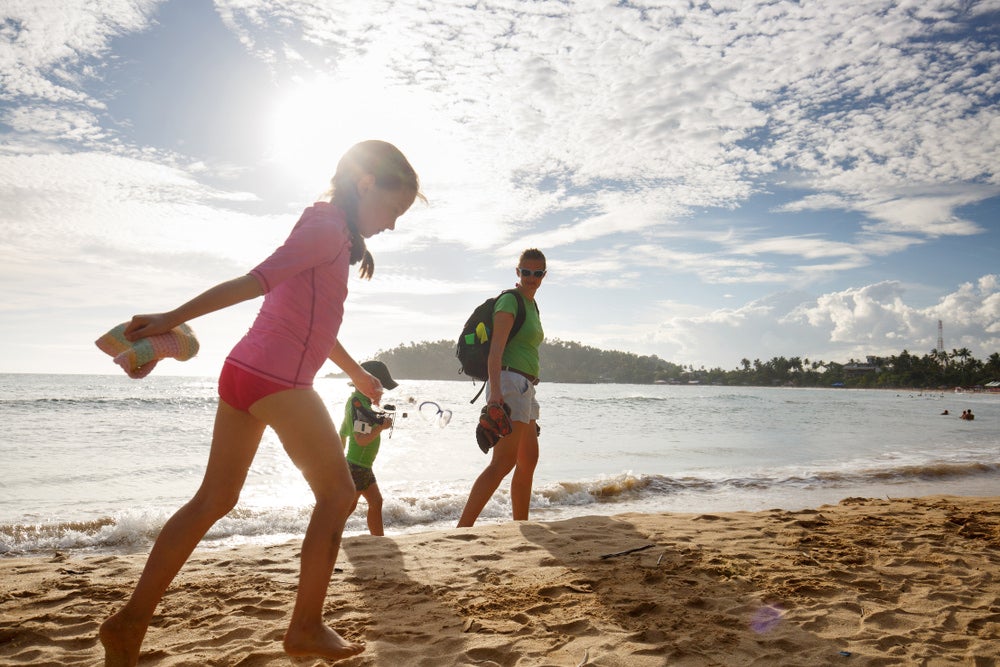 two young kids with parent walking on the beach at sunset