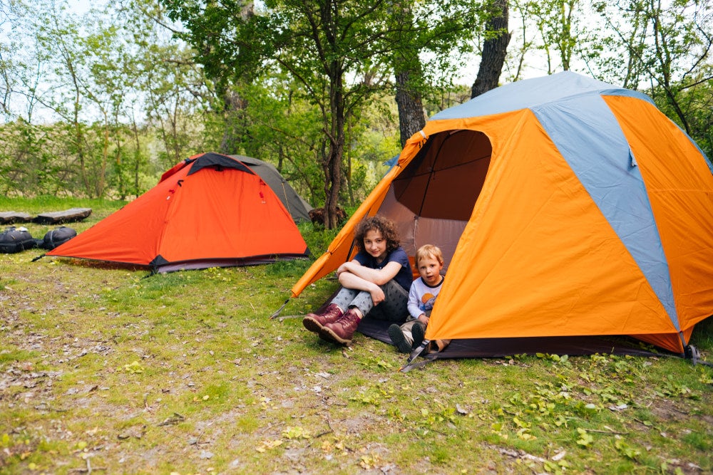 two young children playing in a tent near a second tent at a campground