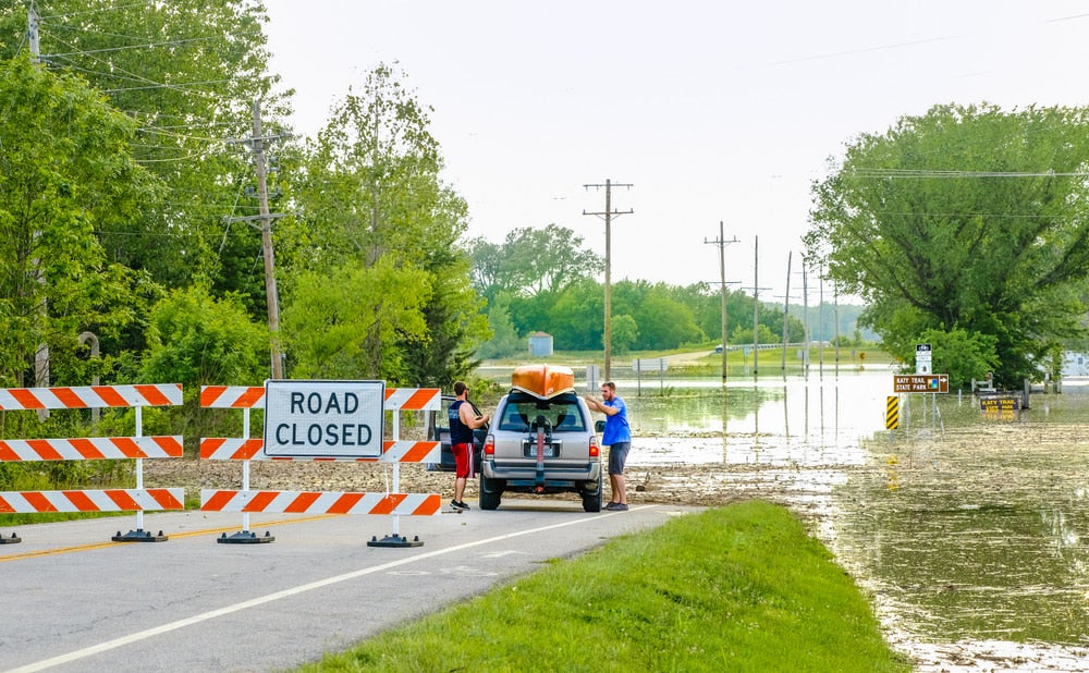 a car near a road block in missouri with a flood flowing over the road