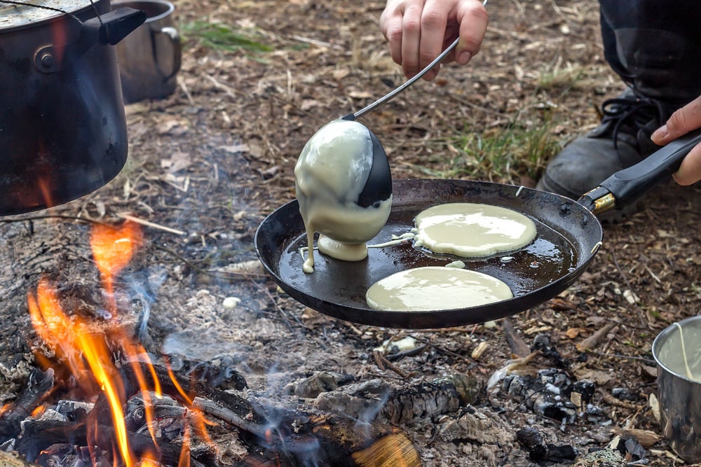 a person pouring pancakes over a campfire