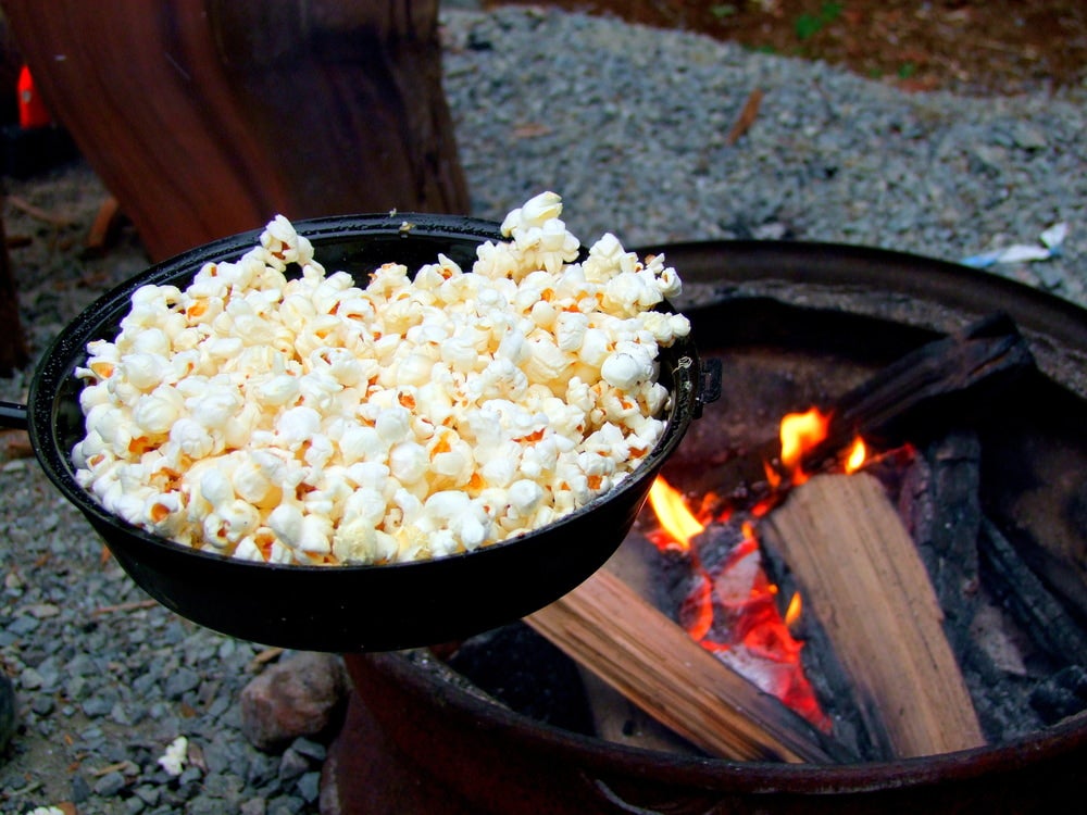popcorn cooking over a campfire in a cast iron