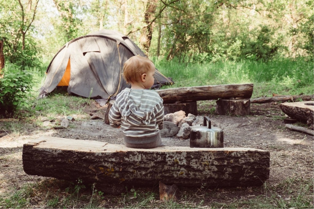 a young boy sitting on a log bench near a campsite