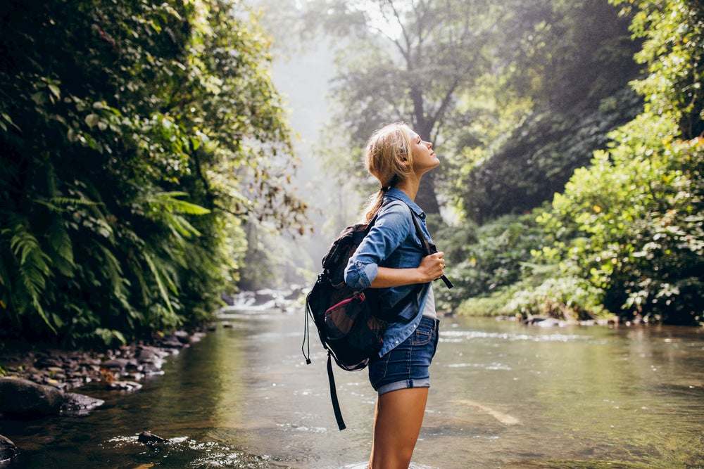 Woman wearing backpack staring upwards with river and trees in background