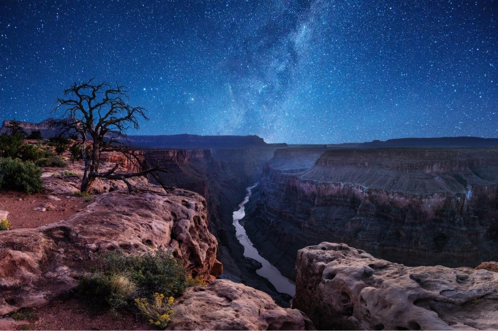 a river running through the grand canyon at night with the milky way above