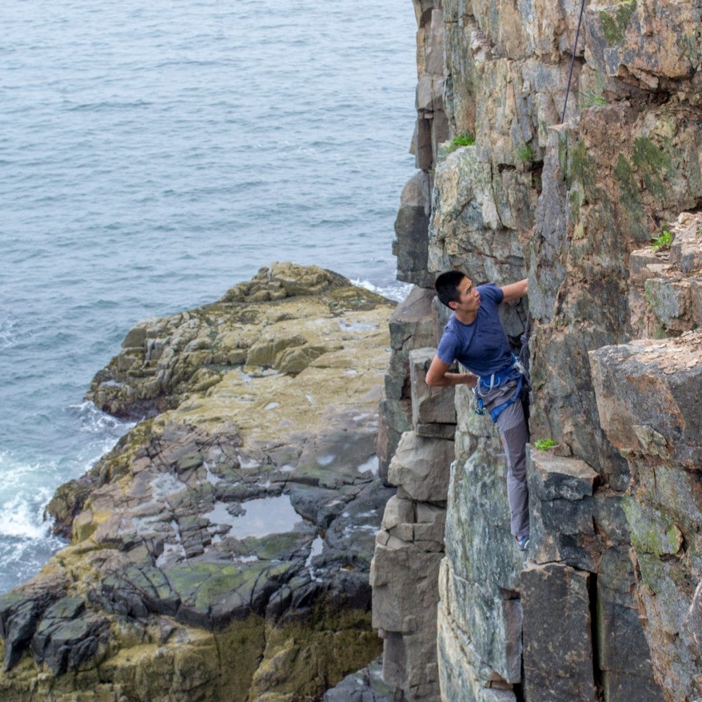 a man paused on a rock wall climbing in acadia national park