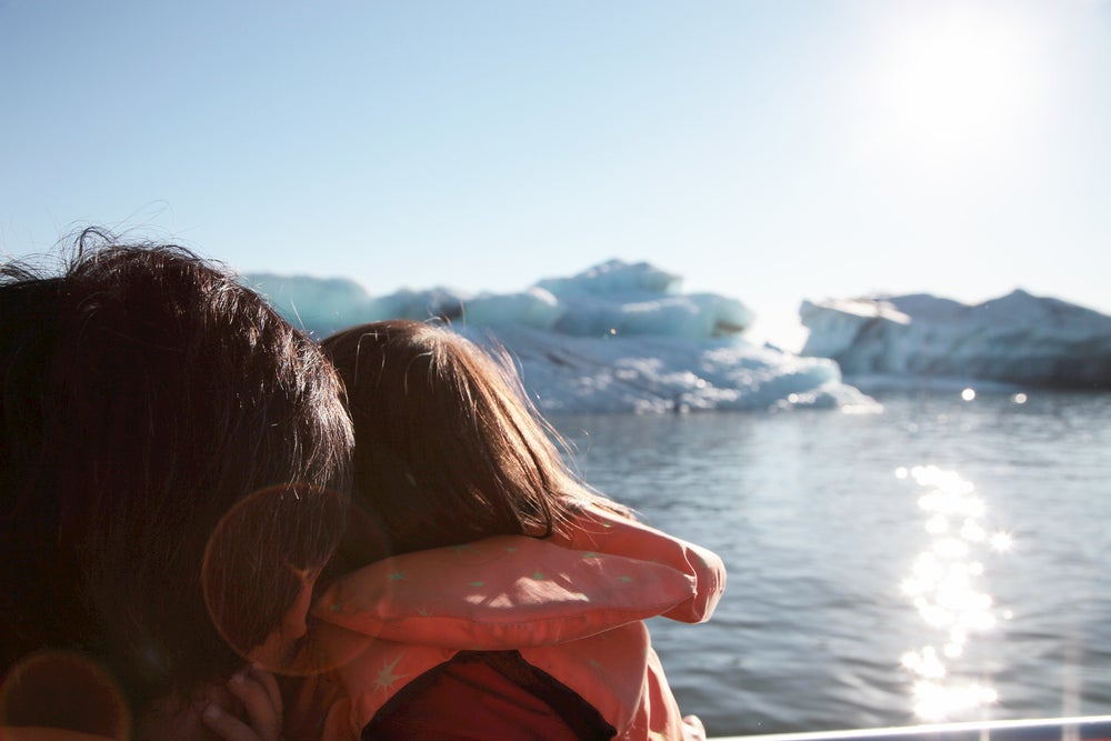 Girl holding on to her father and looking out at glacier in the ocean 