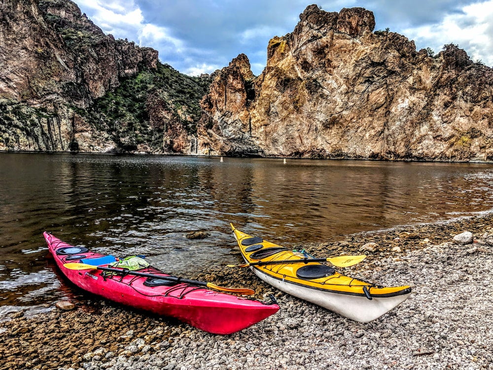 Two kayaks on shore with rock wall in background 