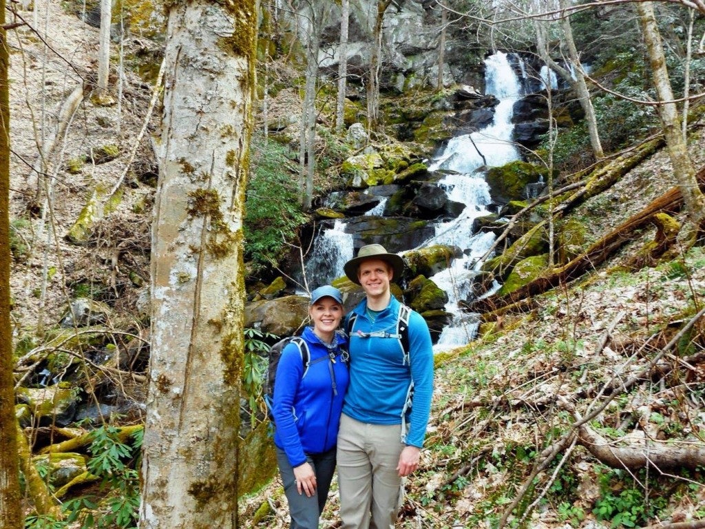 Two people posing with waterfall and trees behind them