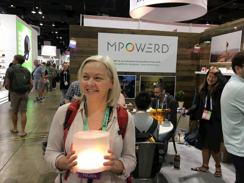 a woman holding a camping light on the show floor of outdoor retailer