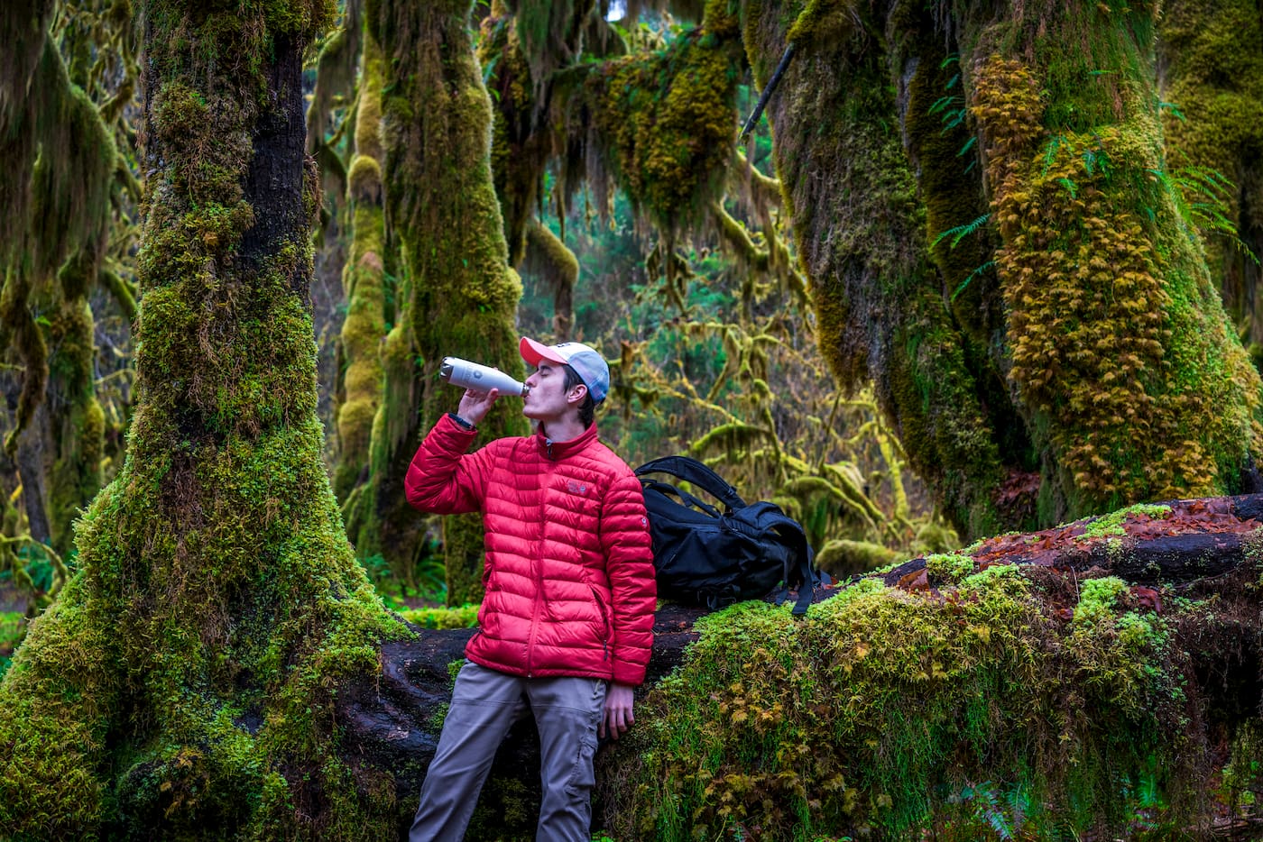 Persona che beve Liquid-IV da una bottiglia d'acqua nella foresta.