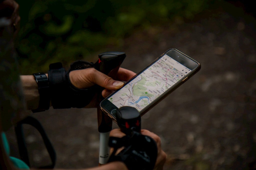 Hiker using trekking poles and hiking app on their smartphone.