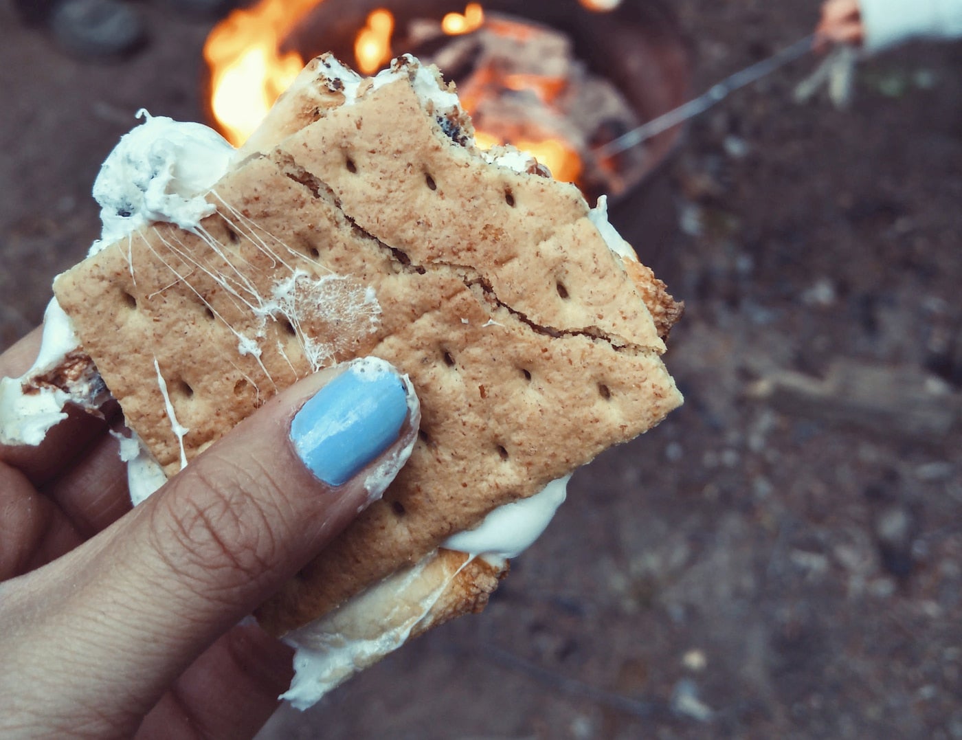 Women holding a s'more in front a a campfire.