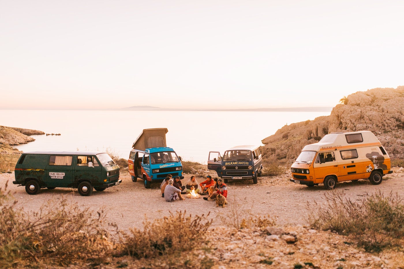 Group of camper vans parked on the edge of the coast at dusk.