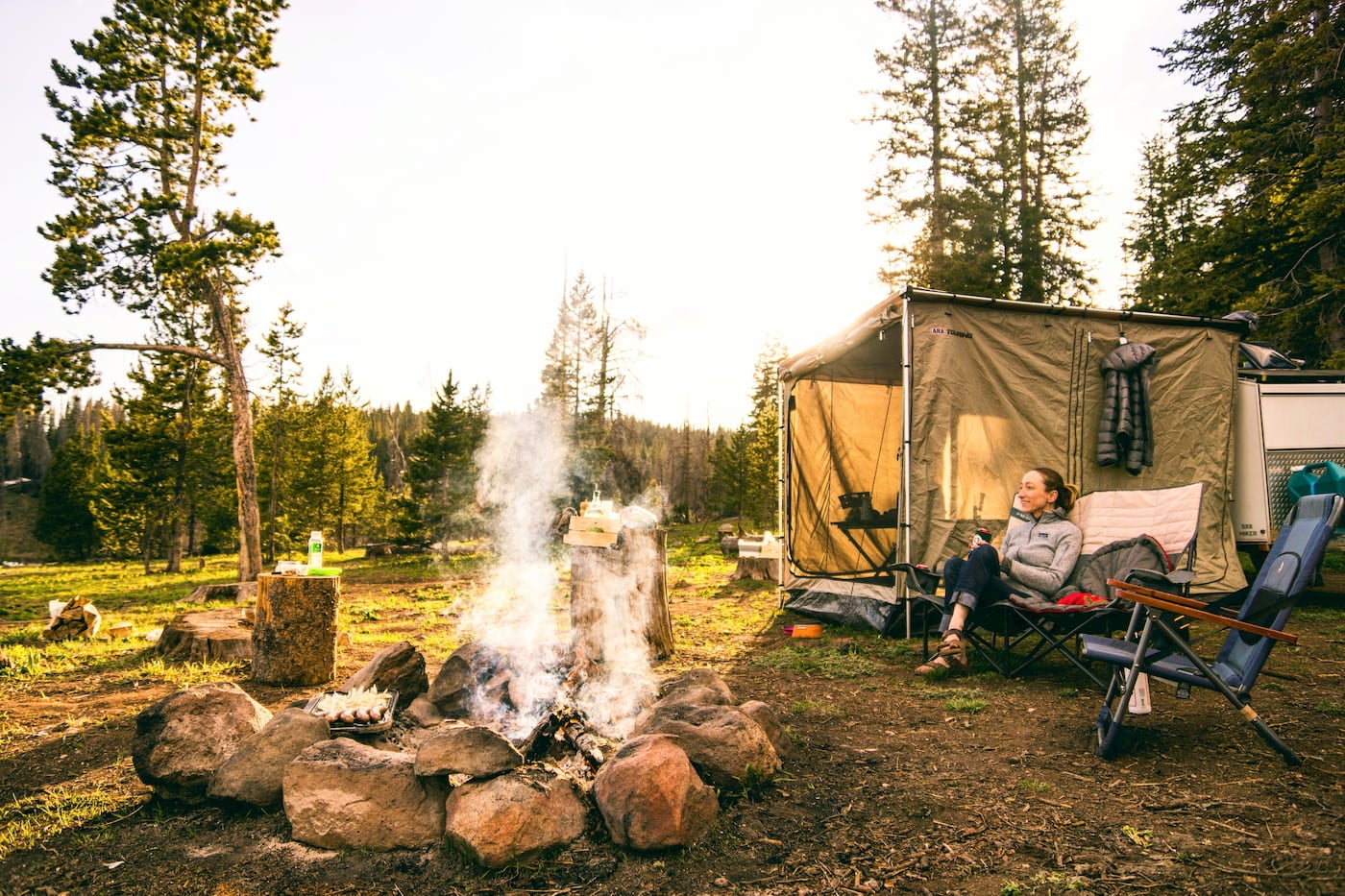 Women lounging beside campfire and tent.