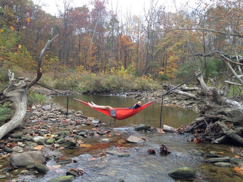 man lounges in red hammock over Cuyahoga Valley calm waters in the fall, photo from a camper on The Dyrt