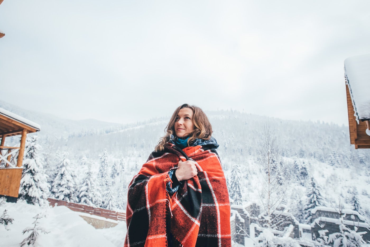 Women wrapped in a red flannel blanket in a snow covered landscape.