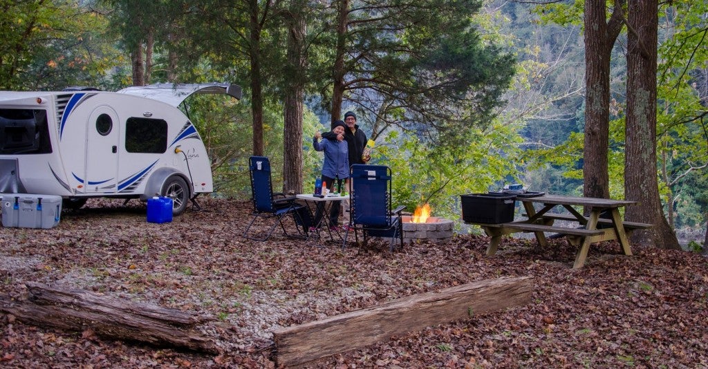 a couple poses for a picture at a campsite with a fire