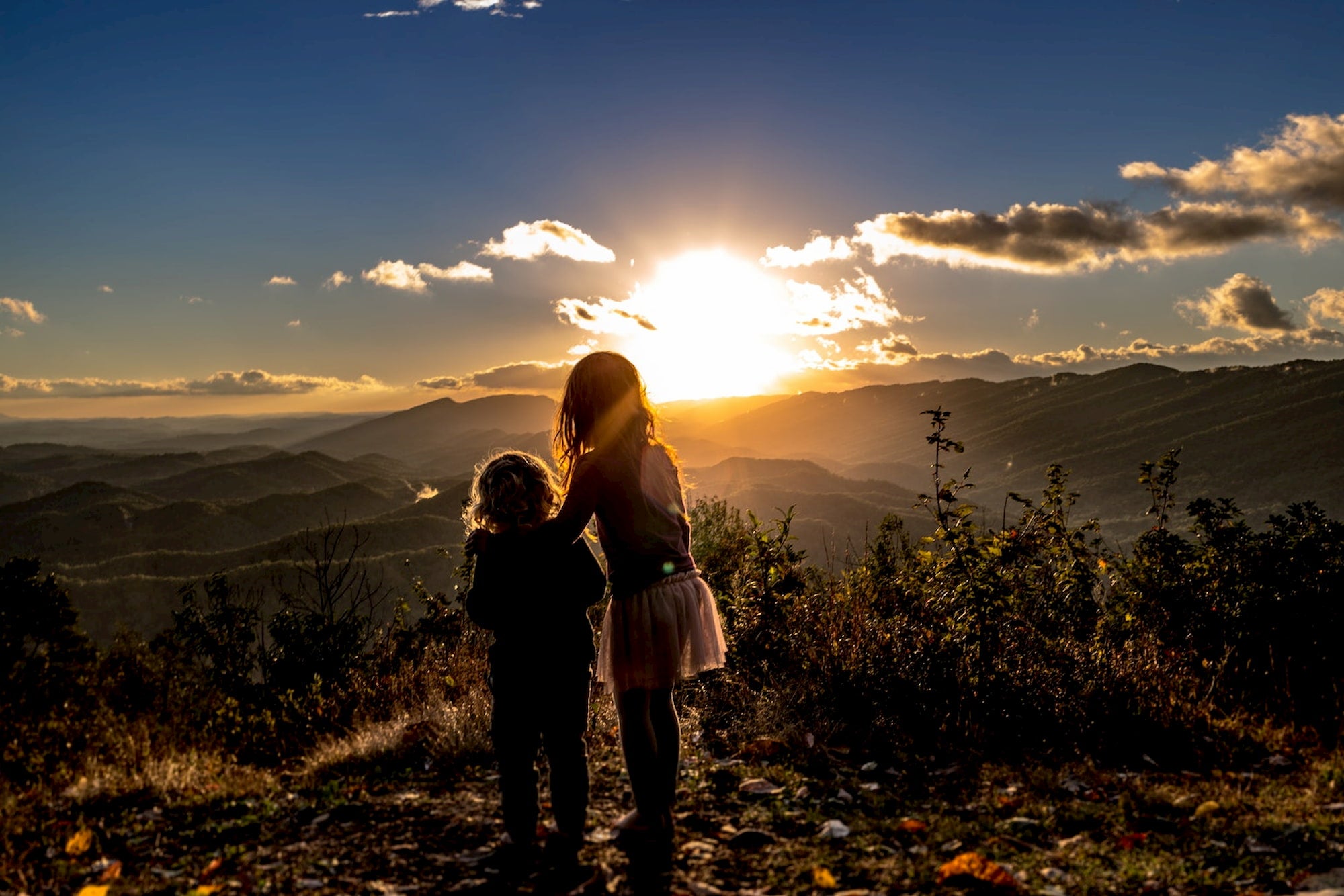 Kids watching the sunset from a mountain.