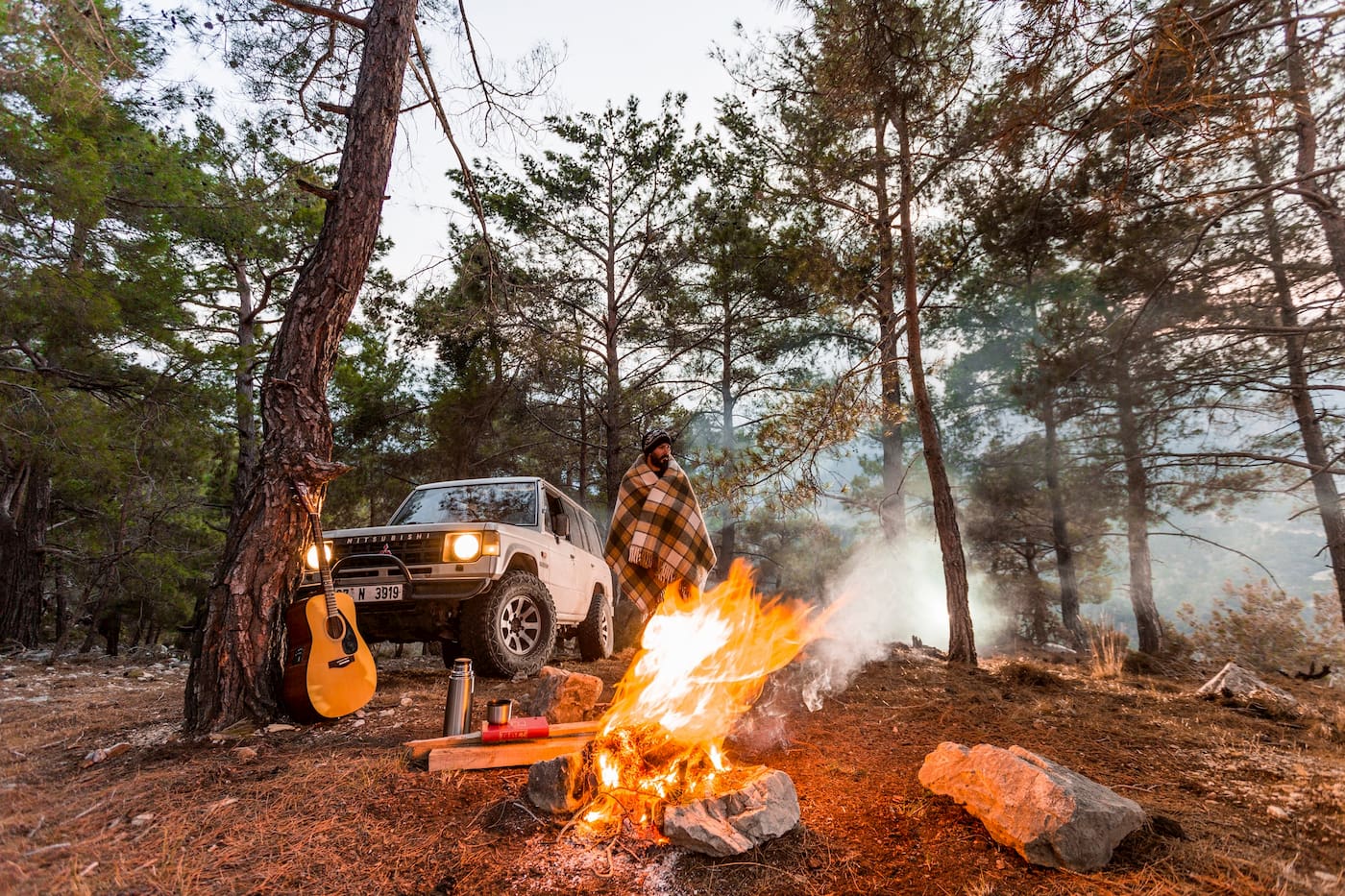 SUV parked in the woods beside a campfire.