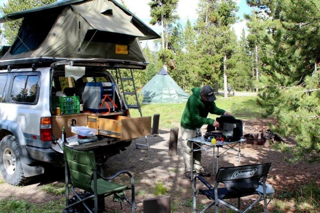 a man at a campground with a car, table and tent set up