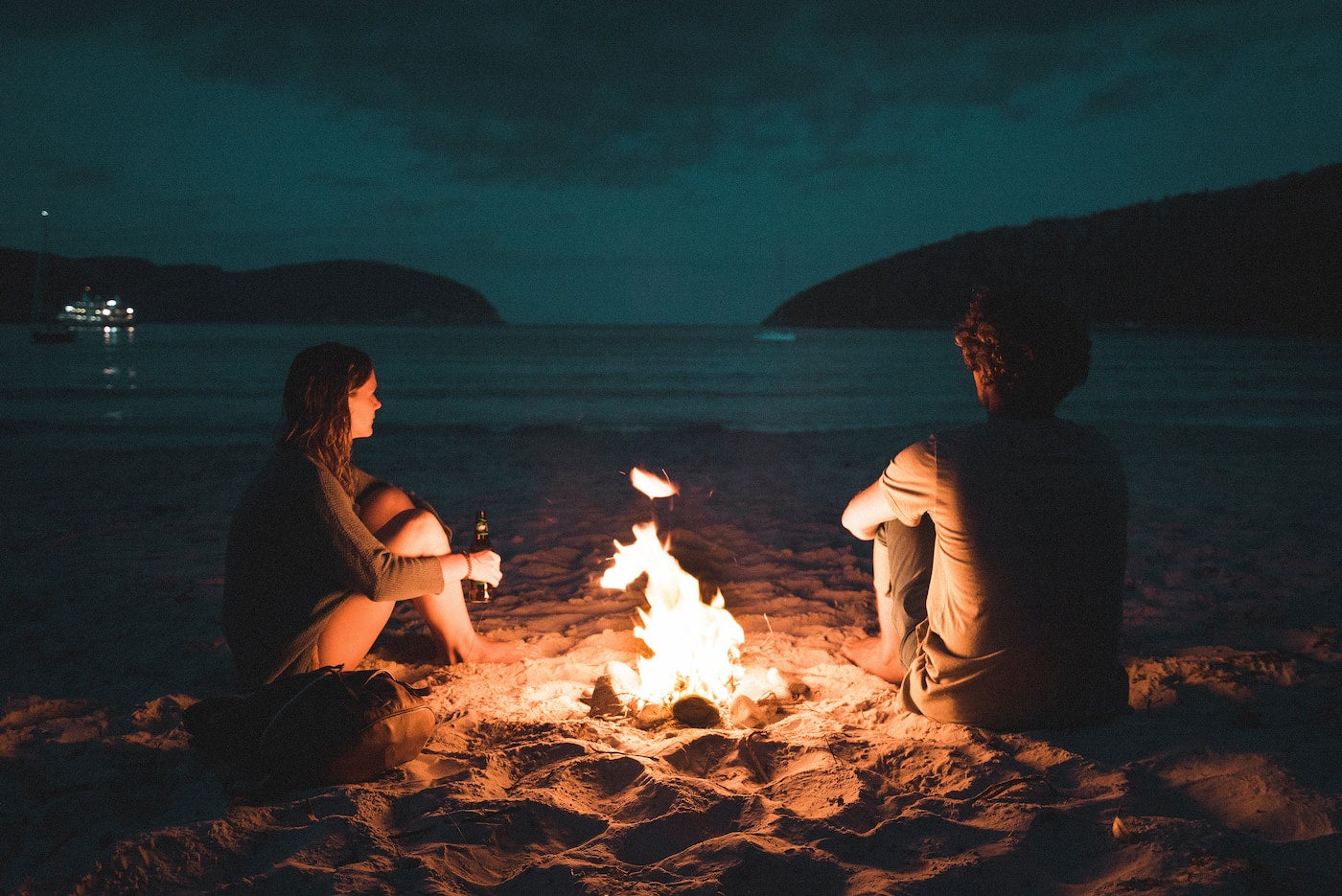 Two people talking and sitting around the campfire.