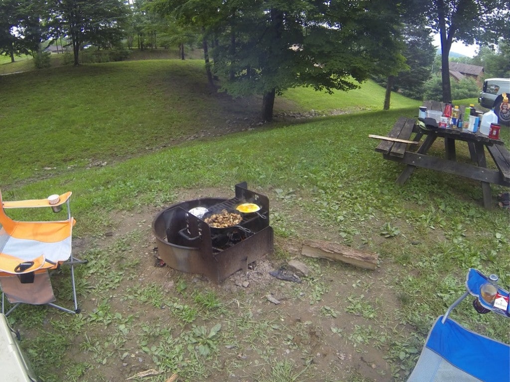 a campfire with two pans cooking food on a grill at a campsite