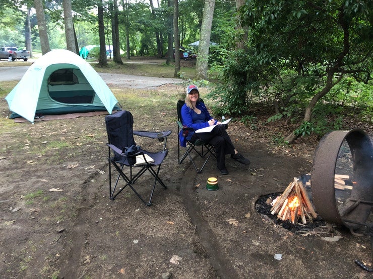 female camper sits between campfire and tent at Rocky Neck State Park, photo from a camper on The Dyrt