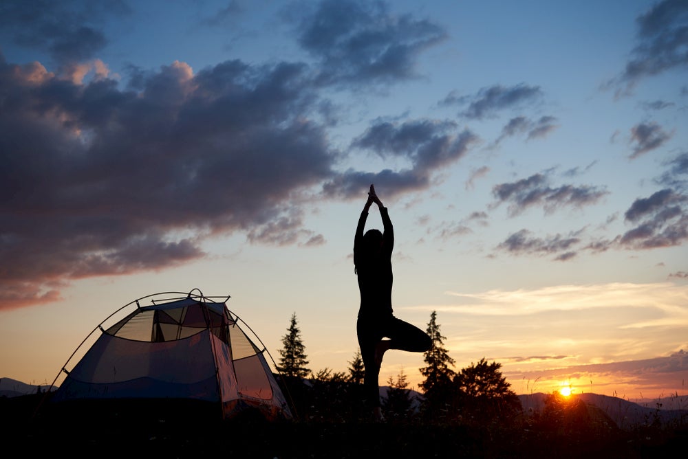 Person doing yoga during dusk beside their tent.