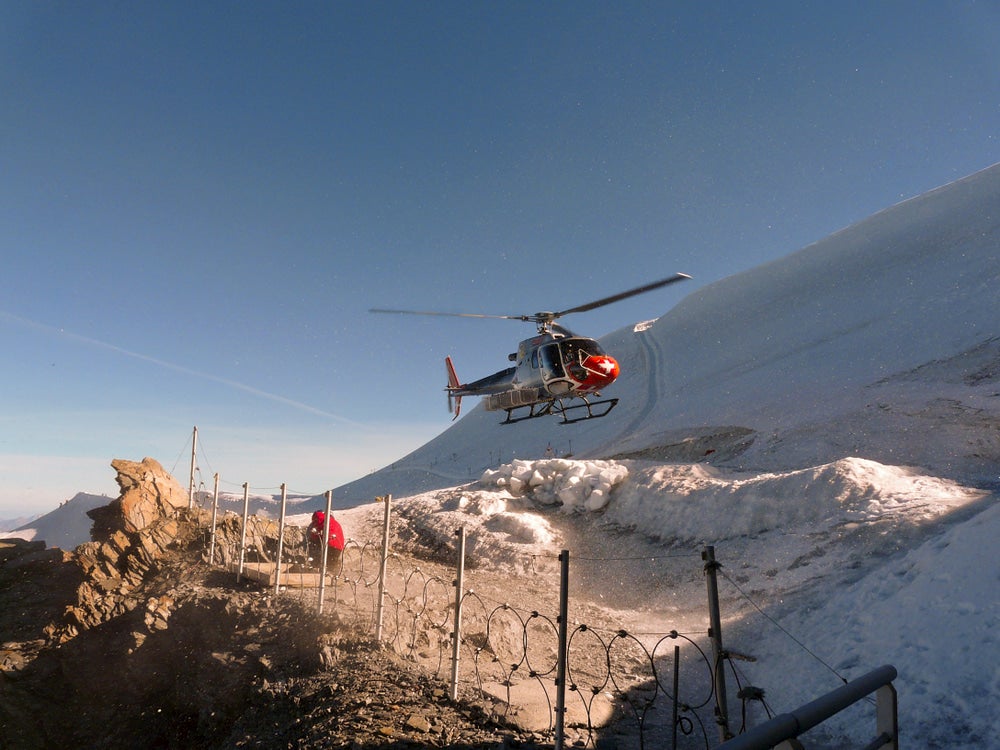 Search and rescue helicopter lifting off on snow covered mountain.