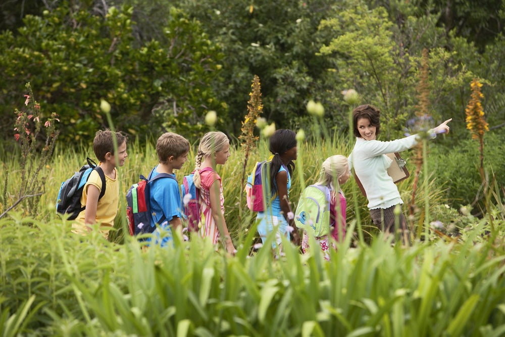 a woman leads a large group of kids in a field during school