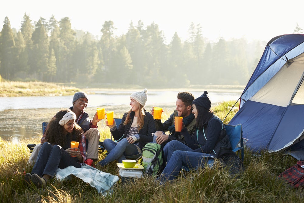 Group of friends hanging out beside a tent drinking out of plastic cups.