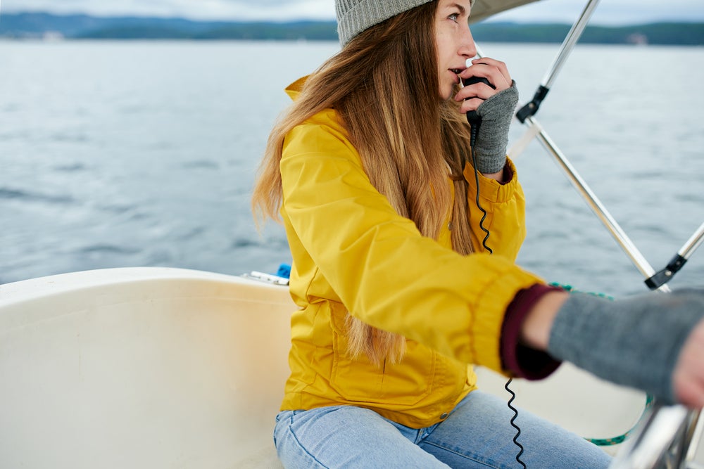 Woman steering a boat while talking into VHF radio.