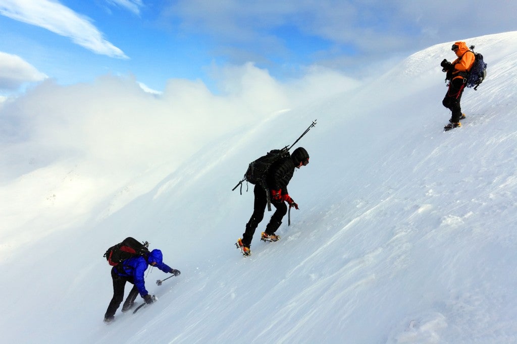 three climbers ascent a snow bank while alpine climbing